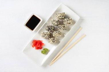 Sushi roll California with salmon, sesame seeds, avocado, cream cheese on white background. Sushi menu, rolls served on white dish with wasabi, ginger and soy sauce. Japanese cuisine food.