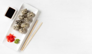 Sushi roll California with salmon, sesame seeds, avocado, cream cheese on white background. Rolls served on white dish with wasabi, ginger and soy sauce. Japanese cuisine food. Top view, copy space