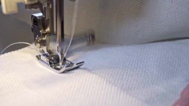 Presser foot and sewing machine needle in motion, process of sewing the fabric. The seamstress sews white fabric in the sewing workshop on modern sewing machine. Professional equipment, tool