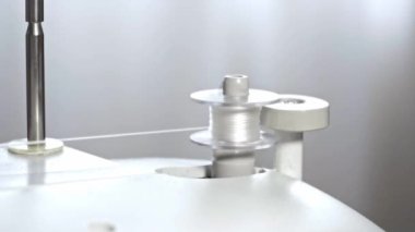 The process of winding thread on the bobbin of a modern sewing machine. Close-up of a spool with white thread. Professional sewing equipment detail, working tool