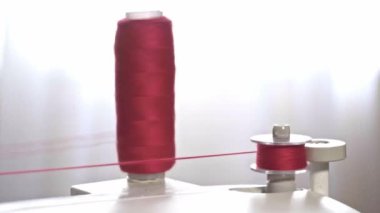 The process of winding thread on the bobbin of a modern sewing machine. Close-up of a spool with red thread. Professional sewing equipment detail, working tool