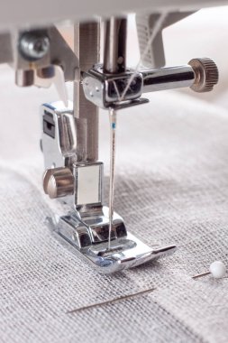 Modern dikiş makinesi, keten kumaşlı ve iplikli ayaklı, yakın plan. İşlem kıyafetleri, perdeler, döşemeler. İş, hobi, el yapımı, sıfır atık, geri dönüşüm, tamir konsepti