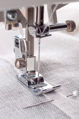 Modern dikiş makinesi, keten kumaşlı ve iplikli ayaklı, yakın plan. İşlem kıyafetleri, perdeler, döşemeler. İş, hobi, el yapımı, sıfır atık, geri dönüşüm, tamir konsepti