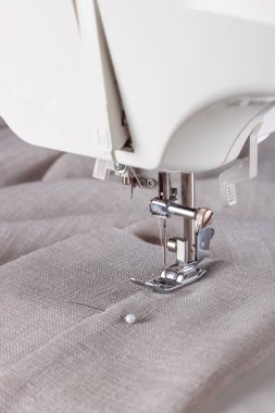 Modern dikiş makinesi, keten kumaşlı ve iplikli ayaklı, yakın plan. İşlem kıyafetleri, perdeler, döşemeler. İş, hobi, el yapımı, sıfır atık, geri dönüşüm, tamir konsepti