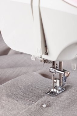 Modern dikiş makinesi, keten kumaşlı ve iplikli ayaklı, yakın plan. İşlem kıyafetleri, perdeler, döşemeler. İş, hobi, el yapımı, sıfır atık, geri dönüşüm, tamir konsepti