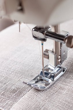 Modern dikiş makinesi, keten kumaşlı ve iplikli ayaklı, yakın plan. İşlem kıyafetleri, perdeler, döşemeler. İş, hobi, el yapımı, sıfır atık, geri dönüşüm, tamir konsepti