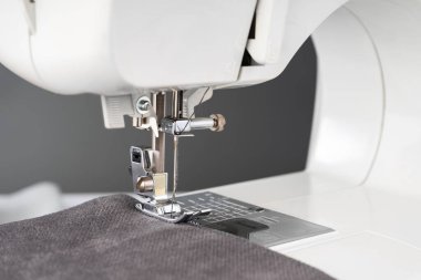 Gri kumaş ve iplikle modern dikiş makinesi ayaklı, yakın plan. İşlem kıyafetleri, perdeler, döşemeler. İş, hobi, el yapımı, sıfır atık, geri dönüşüm, tamir konsepti