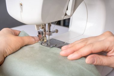 Atölyedeki iş yerindeki modern dikiş makinesine beyaz kumaş diken kadın elleri. Kadın eli, dikiş makinesine kumaş parçaları dikiyor. El yapımı, hobi, küçük işletme konsepti