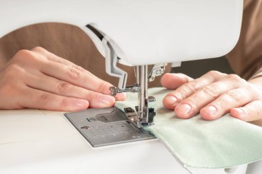 Atölyedeki iş yerindeki modern dikiş makinesine beyaz kumaş diken kadın elleri. Kadın eli, dikiş makinesine kumaş parçaları dikiyor. El yapımı, hobi, küçük işletme konsepti