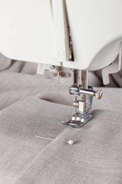 Modern dikiş makinesi, keten kumaşlı ve iplikli ayaklı, yakın plan. İşlem kıyafetleri, perdeler, döşemeler. İş, hobi, el yapımı, sıfır atık, geri dönüşüm, tamir konsepti