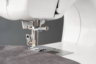 Gri kumaş ve iplikle modern dikiş makinesi ayaklı, yakın plan. İşlem kıyafetleri, perdeler, döşemeler. İş, hobi, el yapımı, sıfır atık, geri dönüşüm, tamir konsepti