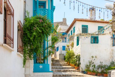 Yazın güneşli bir günde eski Avrupa kasabasında dar bir sokakta. Güzel manzaralı eski beyaz evler, kafeler ve yeşil bitkileri olan dükkanlar. Popüler turizm tatil beldesi, Akdeniz mimarisi