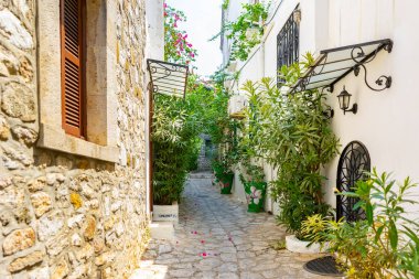 Yazın güneşli bir günde eski Avrupa kasabasında dar bir sokakta. Güzel manzaralı eski beyaz evler, kafeler ve yeşil bitkileri olan dükkanlar. Popüler turizm tatil beldesi, Akdeniz mimarisi