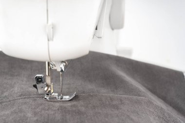 Gri kumaş ve iplikle modern dikiş makinesi ayaklı, yakın plan. İşlem kıyafetleri, perdeler, döşemeler. İş, hobi, el yapımı, sıfır atık, geri dönüşüm, tamir konsepti