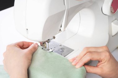 Atölyedeki iş yerindeki modern dikiş makinesine beyaz kumaş diken kadın elleri. Kadın elleri dikiş makinesinin üzerine kumaş parçaları dikiyor. El yapımı, hobi, küçük işletme konsepti