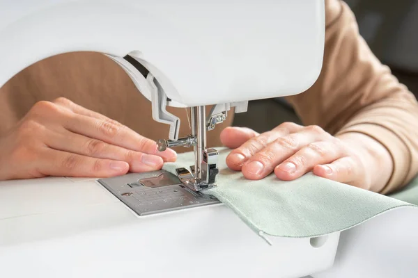 アトリエの職場で現代のミシンに白い布を縫いつける女性の手 女性の手はミシンの上に布を縫いつける 手作り 中小企業のコンセプト — ストック写真