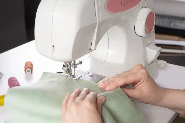 在工作室的现代缝纫机上 女性手工缝制绿色面料 女人的手在缝纫机上缝制面料 业余爱好 小企业概念 — 图库照片