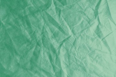 Wrinkled, crumpled green fabric texture background. Wrinkled and creased abstract backdrop of spunbond  textile, wallpaper with copy space, top view.