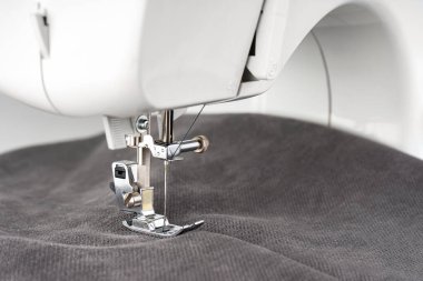 Gri kumaşlı modern dikiş makinesi. İşlem kıyafetleri, perdeler, döşemeler. İş, hobi, el yapımı, sıfır atık, geri dönüşüm, tamir konsepti