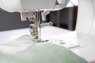 Modern dikiş makinesi ayağıyla yeşil kumaş ve iplik, yakın plan, makro. İşlem kıyafetleri, perdeler, döşemeler. İş, hobi, el yapımı, sıfır atık, geri dönüşüm, tamir konsepti