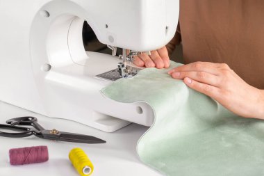 Atölyedeki modern dikiş makinesine yeşil kumaş diken terzi elleri. Kadın elleri dikiş makinesinin üzerine kumaş parçaları dikiyor. El yapımı, hobi, onarım, küçük işletme konsepti