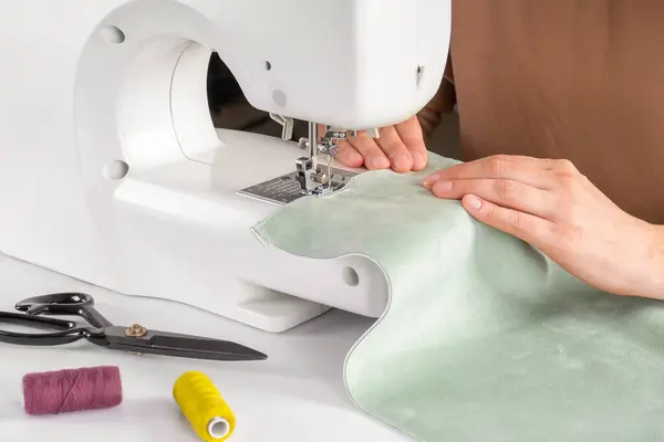 裁缝师在工作室的现代缝纫机上手工缝制绿色面料 妇女的手在缝纫机上缝制面料 业余爱好 小企业概念 免版税图库照片