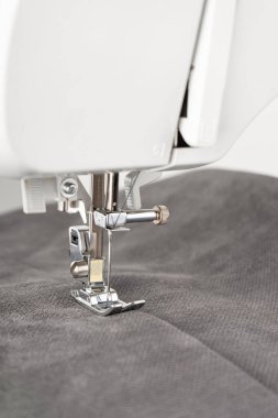 Gri kumaşlı modern dikiş makinesi. İşlem kıyafetleri, perdeler, döşemeler. İş, hobi, el yapımı, sıfır atık, geri dönüşüm, tamir konsepti