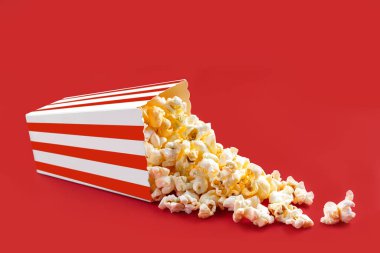Kırmızı çizgili bir karton kutudan ya da kovadan düşen lezzetli peynirli patlamış mısır, kırmızı arka planda izole edilmiş. Patlamış mısır taneleri saçılıyor. Fast food, aperatif. Sinema, sinema ve eğlence konsepti.