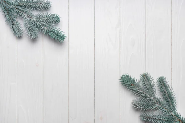 Snowy Christmas fir tree branches on white wooden board background top view, flat lay. Banner, header, wallpaper, backdrop with copy space.