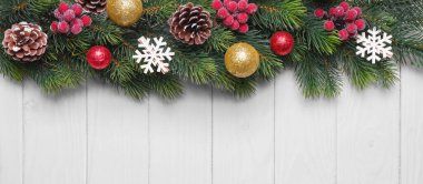 Altın ve yeşil toplarla süslenmiş Noel ağacı dalları, beyaz ahşap arka planda kırmızı bereler ve kar taneleri. Üst görünüm, düz görünüm kopyalama alanı, afiş, başlık, Yeni Yıl arkaplanı