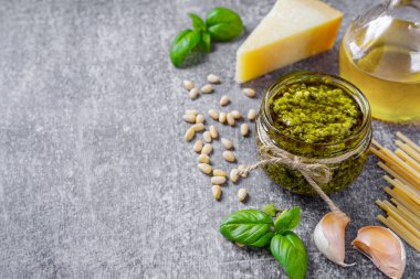 Küçük cam kavanozda ev yapımı pesto sosu ve fotokopi alanı olan gri beton arka planda makarna malzemeleri. Geleneksel İtalyan mutfağı, yemek tarifi, restoran menüsü