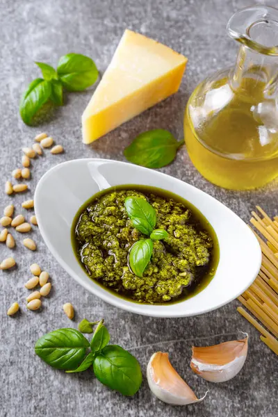 Homemade pesto sauce in small glass jar and ingredients for pasta on gray concrete. Traditional Italian cuisine, recipe, restaurant menu