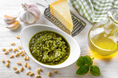 Küçük kavanozda ev yapımı pesto sosu ve beyaz ahşap arka planda makarna malzemesi ve fotokopi alanı. Geleneksel İtalyan mutfağı, yemek tarifi, restoran menüsü