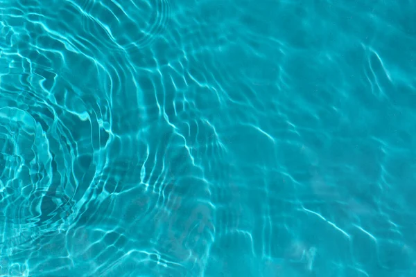 Şeffaf turkuaz berrak su yüzeyi dokusu, güneş ışığında dalgalar, dalgalar ve halkalar. Soyut doğa su arka planı, güneşli yansımalar 