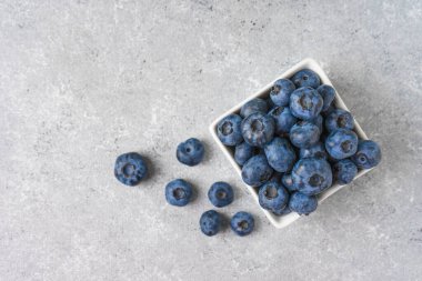 Fotokopi alanı olan gri beton arka planda küçük kare bir kasede taze yaban mersini. Organik böğürtlen, sağlıklı yiyecek, yabanmersini. Üst manzara, düz uzanma