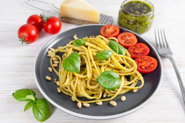 Makarna pesto, pesto soslu spagetti ve besin maddeleriyle servis edilen beyaz ahşap arka planda siyah tabakta taze fesleğen yaprakları. Geleneksel İtalyan mutfağı.