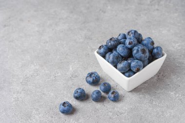 Küçük, kare beyaz bir kasede taze yaban mersini. Fotokopi alanı olan gri beton arka planda böğürtlen serpiştirilmiş. Organik böğürtlen, sağlıklı yiyecek, yabanmersini.