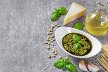 Küçük beyaz yuvarlak kavanozda ev yapımı pesto sosu ve gri taş beton üzerinde makarnanın malzemeleri ve fotokopi alanı. Geleneksel İtalyan mutfağı, yemek tarifi, restoran menüsü