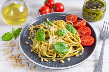 Makarna pesto, pesto soslu spagetti ve besin maddeleriyle servis edilen beyaz ahşap arka planda siyah tabakta taze fesleğen yaprakları. Geleneksel İtalyan mutfağı.