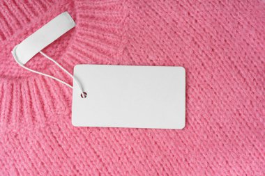 Pembe örülmüş süveter arka planında iç etiketi ve boş kıyafet etiketi var. Fiyat ya da metin için boş dikdörtgen kartlı şablon. Alışveriş, indirim, kara cuma, moda.