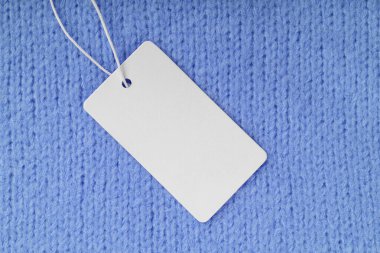 Mavi örgü süveter arka planında boş kıyafet etiketi var. Model, boş dikdörtgen kartlı şablon, fiyat ya da metin için kumaş etiket. Alışveriş, indirim, kara cuma, moda konsepti..