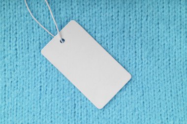 Turkuaz örgü süveter arka planında boş kıyafet etiketi. Model, boş dikdörtgen kartlı şablon, fiyat ya da metin için kumaş etiket. Alışveriş, indirim, kara cuma, moda konsepti..