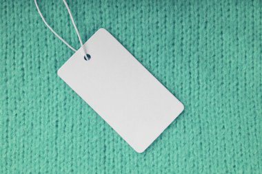 Yeşil örgü süveter arka planında boş kıyafet etiketi. Model, boş dikdörtgen kartlı şablon, fiyat ya da metin için kumaş etiket. Alışveriş, indirim, kara cuma, moda konsepti..