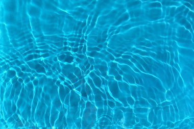 Şeffaf mavi berrak su yüzeyi dokusu, güneş ışığında dalgalar, dalgalar ve halkalar. Soyut doğa su arka planı, güneşli yansımalar 