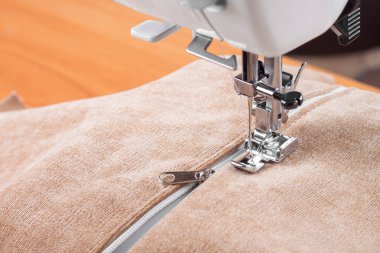 Modern dikiş makinesi bej kumaşlı, iplikli, özel presser ayaklı, yakın plan. Fermuara dikiş dikme işlemi. İş, hobi, el yapımı, sıfır atık, geri dönüşüm, tamir konsepti.