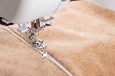 Modern dikiş makinesi bej kumaşlı, iplikli, özel presser ayaklı, yakın plan. Fermuara dikiş dikme işlemi. İş, hobi, el yapımı, sıfır atık, geri dönüşüm, tamir konsepti.