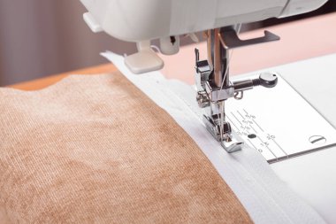 Modern dikiş makinesi bej kumaşlı, iplikli, özel presser ayaklı, yakın plan. Fermuara dikiş dikme işlemi. İş, hobi, el yapımı, sıfır atık, geri dönüşüm, tamir konsepti.