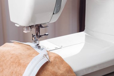 Modern dikiş makinesi bej kumaşlı, iplikli, özel presser ayaklı, yakın plan. Fermuara dikiş dikme işlemi. İş, hobi, el yapımı, sıfır atık, geri dönüşüm, tamir konsepti.