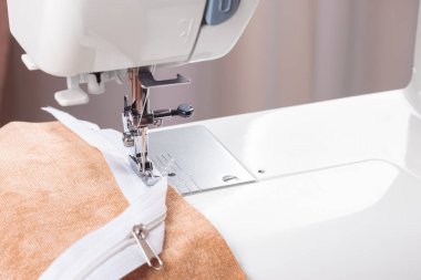 Modern dikiş makinesi bej kumaşlı, iplikli, özel presser ayaklı, yakın plan. Fermuara dikiş dikme işlemi. İş, hobi, el yapımı, sıfır atık, geri dönüşüm, tamir konsepti.