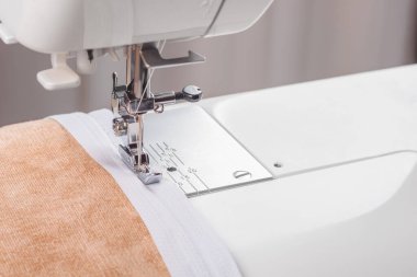 Modern dikiş makinesi bej kumaşlı, iplikli, özel presser ayaklı, yakın plan. Fermuara dikiş dikme işlemi. İş, hobi, el yapımı, sıfır atık, geri dönüşüm, tamir konsepti.